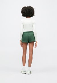 Πράσινα σορτς με κορδόνι στη μέση, συνδυασμένα με λευκό τοπ μακρυμάνικο. Τα σορτς έχουν μαλακή υφή και άνετη εφαρμογή.