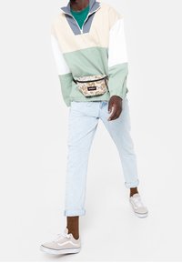 Sportowa kurtka w blokach kolorystycznych: beżowy, miętowy i szary; jasnoniebieskie jeansy; beżowe sneakersy; wzorzysty nerka. Casualowy, luźny krój.