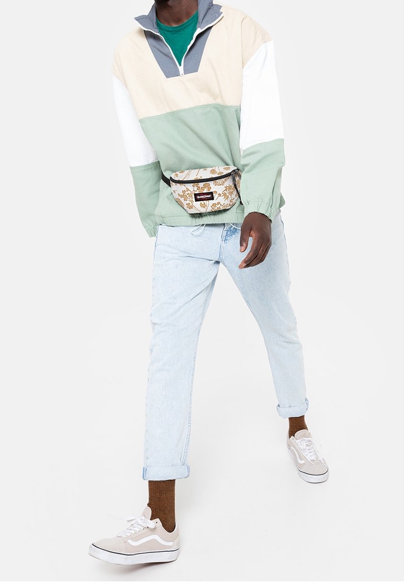 Giacca sportiva a blocchi di colore in beige, menta e grigio; jeans azzurri; sneakers beige; marsupio con motivo a fantasia. Vestibilità casual e rilassata.