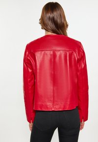 Rød læderjakke med et cropped design, der har en lige pasform, glat tekstur og syningdetaljer. Lange ærmer med sidesømme.