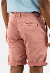 Shorts di cotone rosa con risvolti, dotati di tasche posteriori e un'etichetta con il logo. Texture liscia e vestibilità su misura.