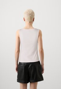 Lys rosa ermeløs topp med ribbet tekstur og rund halslinning, paret med svarte faux skinnshorts med sidelommer og rullede mansjetter.