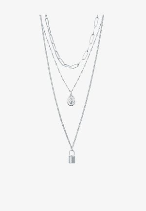 Trois colliers argentés superposés avec différents styles de chaînes, l'un avec un pendentif œil et un autre avec un petit pendentif cadenas.