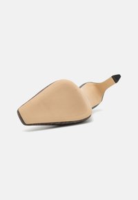 Zapato de tacón alto negro con punta afilada, presenta una suela texturizada en color beige y una parte superior de cuero suave. El tacón es delgado y está en ángulo.
