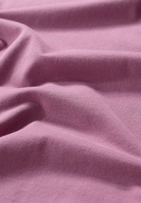 Puuvillakangas pehmest hallikasroosast toonist, millel on sile tekstuur, kergete voldide ja kortsudega, mis loovad orgaanilise langevuse.