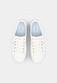 Pair of white Tommy Hilfiger sneakers with gold eyelets and light blue insoles, viewed from above against a white background.