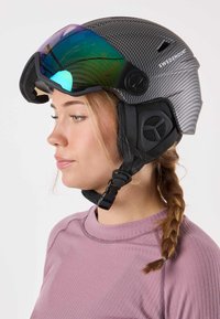 Helmet with a carbon fiber texture, black finish, oversized visor with iridescent tint, adjustable chin strap, and padded ear covers.