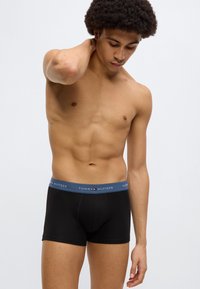Μαύρα ανδρικά βαμβακερά εσώρουχα με μπλε ζώνη μέσης που φέρει το λογότυπο "TOMMY HILFIGER" σε λευκό. Ομαλή υφή, εφαρμοστός σχεδιασμός, μέσο μήκος.