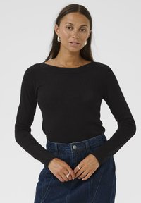 Zwarte langemouwen top met een wijde halslijn en een aansluitend ontwerp. Het materiaal lijkt zacht; gecombineerd met een denimrok met knoopdetails.