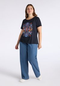 Svart t-shirt med färggård broderi mönster, rundad hals, korta ärmar, kombinerad med ljusblå vida jeans och vita sneakers.