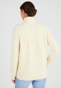 Suéter de cuello alto en color crema con un diseño de tejido texturizado, que cuenta con un dobladillo acanalado y mangas largas. Material suave y acogedor, adecuado para el clima más fresco.