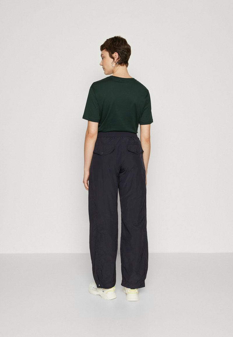 Donkergroene shirt met korte mouwen, gecombineerd met loszittende zwarte broeken met zijzakken, gemaakt van een lichtgewicht, gladde stof.