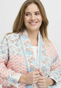 Sciarpa colorata a motivi con intricati design floreali e geometrici in blu e corallo, realizzata in tessuto leggero con una consistenza morbida.