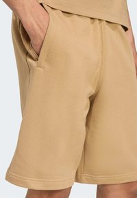Beige bomuldsbukser med elastisk talje, sidelommer og afslappet pasform. Har en glat tekstur og lige ben design.