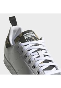 Vit lädersneaker med camouflagemönstrade detaljer, platta vita skosnören, perforeringar på sidan och en märkt tungetikett.