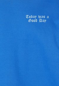 Kék pamut póló fehér felirattal: "Ma jó nap volt." Sima textúrájú, testhez simuló kialakítás.