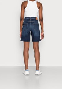 Jeansowe szorty w ciemnoniebieskim kolorze z lekko postarzanym wykończeniem, wyposażone w tylne kieszenie oraz jasnobrązową skórzaną naszywkę powyżej pasa.
