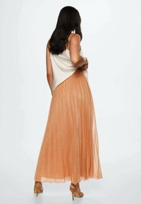 Letto plisseret nederdel i metallisk fersken, parret med en crèmelignende satin top. Har en tætsiddende talje og et svajet, ankel-langt design.