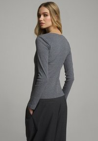 Dopasowana szara bluzka z długim rękawem z miękkiego materiału, z okrągłym dekoltem i elegancką sylwetką, połączona z czarnymi spodniami z kieszeniami.