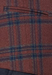 Tkanina w kratkę z bordo jako podstawowym kolorem, z niebieskimi i szarymi liniami. Teksturowane sploty z detalem kieszeni na piersi. Ciemniejsza niebieska tkanina poniżej.