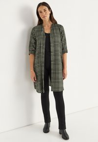 Grünes karierter Langarmhemd mit Kragen, Knopfverschluss, hochgerollten Ärmeln, kombiniert mit schwarzen Leggings und Stiefeletten.