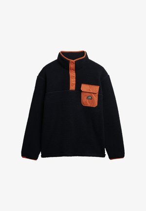 Polarowy półgolf w kolorze granatowym z pomarańczowym kołnierzykiem i kieszonką na piersi. Posiada zamek błyskawiczny na ćwierć długości oraz teksturowany materiał, zapewniający ciepło i komfort.