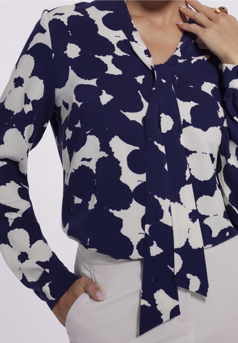 Blouse bleu marine avec un motif floral blanc, manches longues et décolleté en V. Dotée d'un lien au niveau du col et d'un tissu lisse et léger.