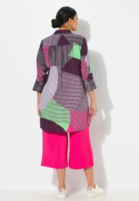 Tunic lunga con base viola e motivi geometrici in rosa, verde e bianco, abbinata a culottes rosa brillante. Il materiale sembra leggero.