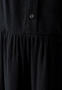 Abito nero caratterizzato da un tessuto texturizzato, design plissettato e un singolo bottone argentato all'collo, che enfatizza una silhouette fluida.