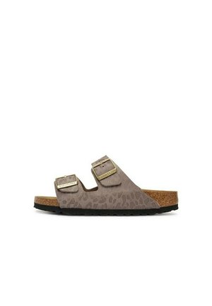 Bruine suède slidesandaal met twee verstelbare goudkleurige gespen en een kurken voetbed op een zwarte zool.