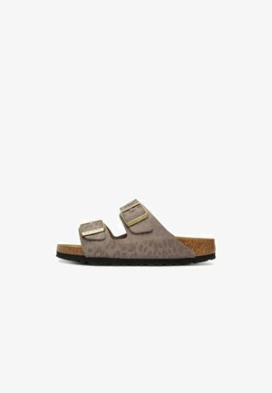 Bruine suède slidesandaal met twee verstelbare goudkleurige gespen en een kurken voetbed op een zwarte zool.
