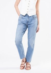 Lichtblauwe denim jeans met een comfortabele pasvorm, vijf zakken en een vervaagd textuur; gecombineerd met bruine sleehakken met bandjes.