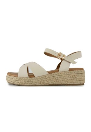 Beige wedge sandal with braided jute platform, crisscross straps, and adjustable ankle strap with gold buckle.