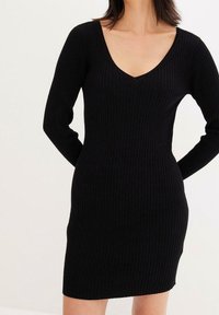 Svart ribbat stickat klänning med långa ärmar, en V-ringning och en figurnära silhuett, tillverkad av mjukt, elastiskt tyg för komfort.