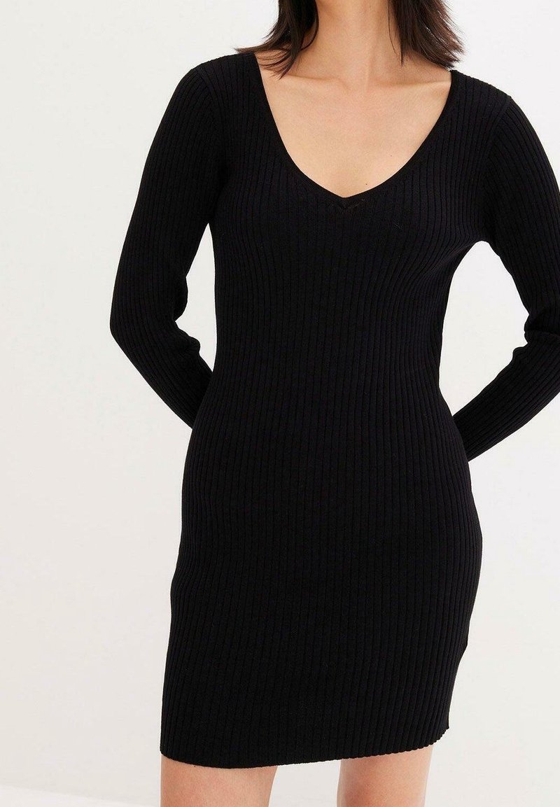 Svart ribbat stickat klänning med långa ärmar, en V-ringning och en figurnära silhuett, tillverkad av mjukt, elastiskt tyg för komfort.