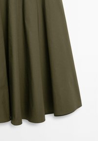 Jupe en coton vert olive avec un design évasé, présentant une texture lisse, des lignes épurées et un ourlet arrondi.