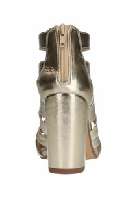 Metalen gouden hoge hak schoen met een corset-achtige ontwerp, voorzien van een rits aan de achterkant en uitgesneden banden. Glad textuur en chunky hak.