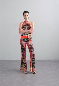 Ensemble coloré en deux pièces comprenant un top halter et un pantalon évasé avec des motifs abstraits en rouge, noir et vert, fabriqué à partir de tissu léger.