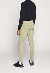 Light green chinos with a slim fit, featuring back pockets and a smooth texture, paired with a black long-sleeve shirt and black sneakers.