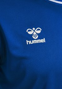 Blå textilskjorta med en vit "hummel"-logotyp och designaccenter. Materialet verkar jämnt med en lätt lyster.