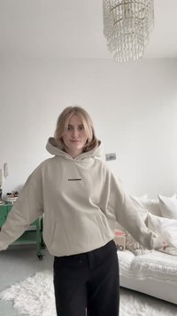 Beige hoodie with front pocket and drawstring hood, featuring "PEGADOR" text in black. Worn with black pants, against a light background.