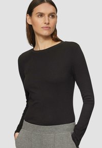Zwarte ribbeltrui met lange mouwen, een ronde halslijn, een aansluitend ontwerp en een zachte textuur, gecombineerd met grijze high-waisted broek.