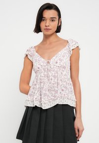 Μπλούζα με μοτίβο λουλουδιών, κοντά μανίκια σε ανοιχτό ροζ και λευκό χρώμα, με V-λαιμόκοψη, σφιγμένη μέση και βολάν στη βάση. Συνδυασμένη με μαύρη φούστα.