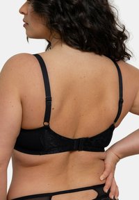 Soutien-gorge noir avec des accents en dentelle, des bretelles ajustables et une fermeture à crochets. Il présente une texture lisse et un design structuré.