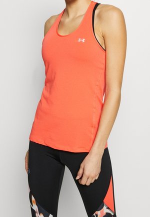 Woman wearing a bright orange sleeveless athletic top with black and patterned leggings, standing against a plain background.