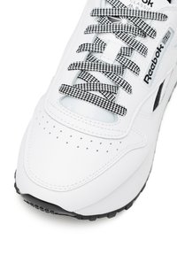 Fehér sneaker perforált orr résszel, textúrált fekete-fehér kockás fűzőkkel és diszkrét márkázási részletekkel az oldalon. Fekete gumitalp.