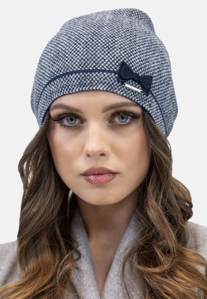 Knitted blue and white patterned beanie featuring a decorative navy bow and a silver accent. Soft texture, rounded top design.