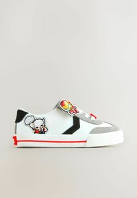Zapatilla deportiva de lona blanca con detalles en gris, suela roja y parches de personajes divertidos en los laterales. Presenta un diseño sin cordones pero con lazos decorativos.