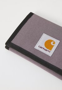 Šedá látková peněženka s černým prošíváním, která obsahuje bílou nášivku s logem Carhartt a oranžovými akcenty. Texturovaný povrch s obdélníkovým tvarem.