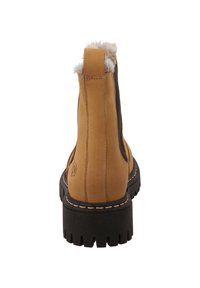 Bottines en suède marron avec un panneau latéral élastique noir uni, un col en fausse fourrure et une semelle en caoutchouc épaisse et texturée avec un motif de crampons.